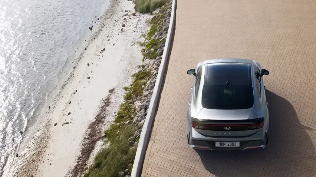 Overhead view of a 2026 Hyundai Sonata driving beside a shoreline road with a clean, sculpted roofline.