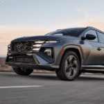 2026 Hyundai Tucson compact SUV driving on highway at dusk, front three quarter exterior view.