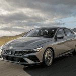 2026 Hyundai Elantra sedan driving on an open highway, front three-quarter view highlighting sleek exterior design and aerodynamic profile.