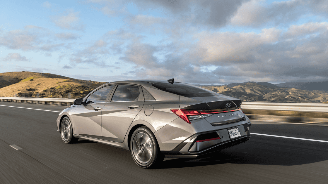 2026 Hyundai Elantra rear three quarter exterior driving on highway with scenic hills.