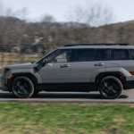 2026 Hyundai Santa Fe SUV driving in profile view on a paved road, showcasing bold body lines, black wheels, and rugged midsize styling.