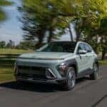 2026 Hyundai Kona compact SUV driving on a rural road, highlighting updated front styling, LED lighting, and aerodynamic profile.