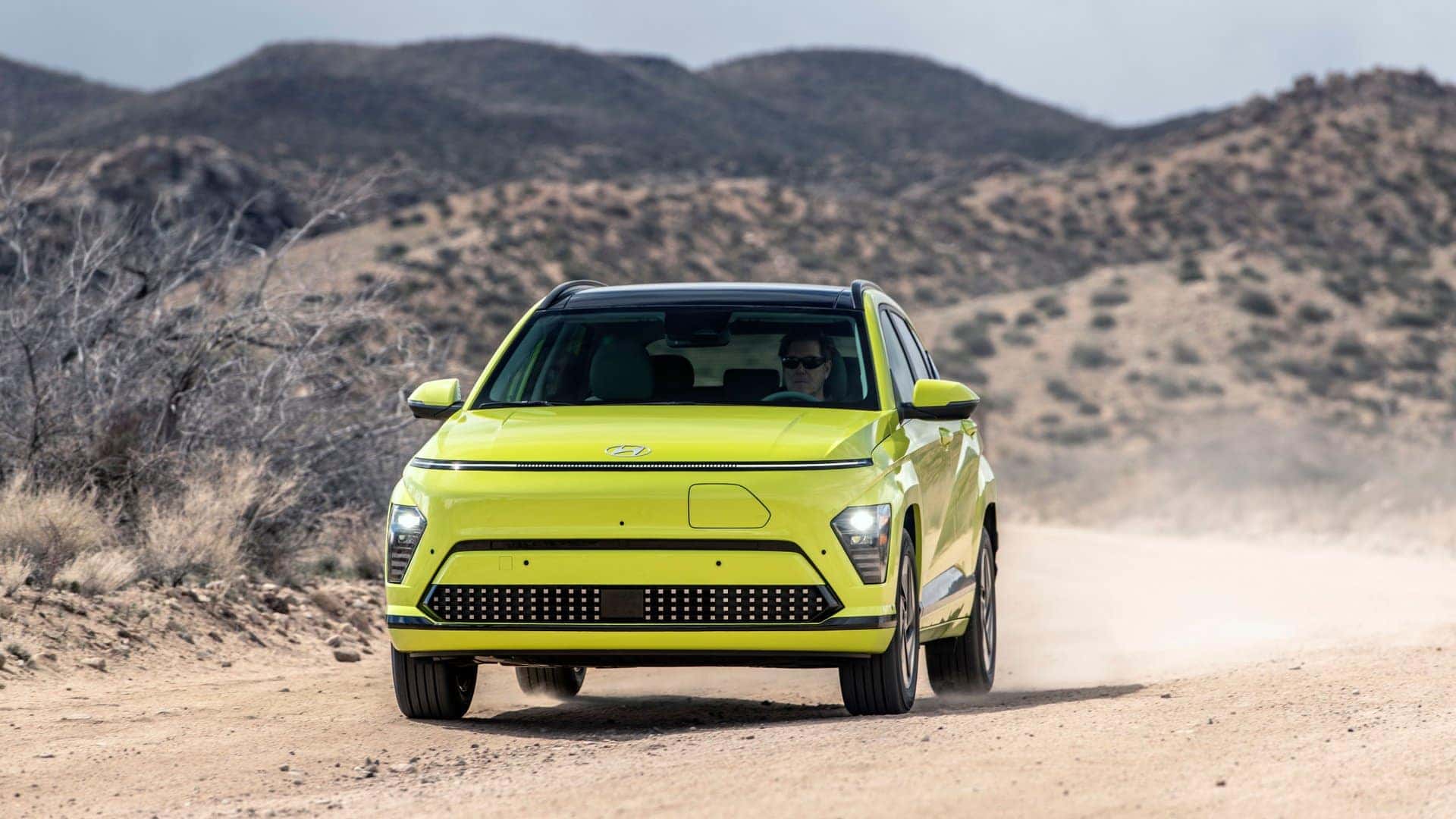2025 Hyundai Kona Electric compact SUV driving on a dirt road through a desert landscape.