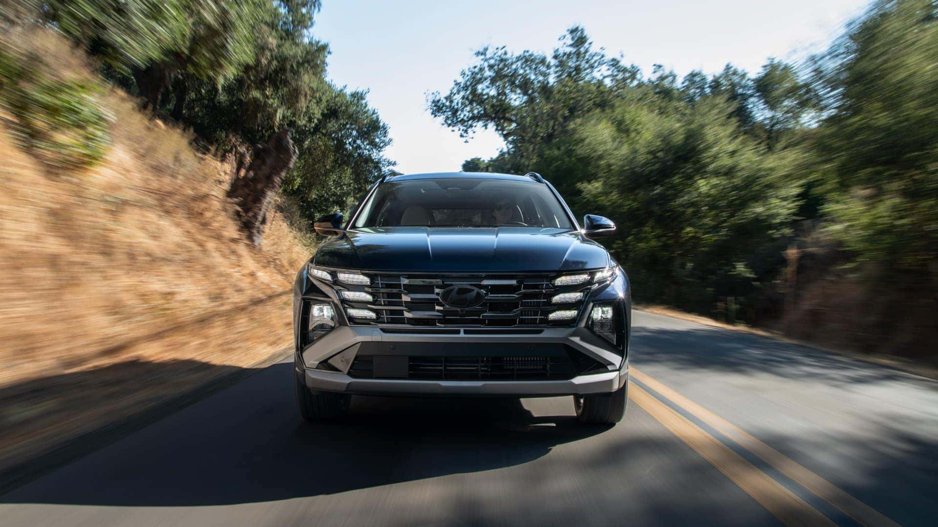 2026 Hyundai Tucson Hybrid SUV driving on a scenic forest road with modern LED headlights.