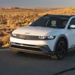 2026 Hyundai IONIQ 5 electric SUV driving on a desert highway in front three quarter view.