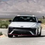 2026 Hyundai Elantra N white sport sedan driving on desert road with front grille and red accent trim.