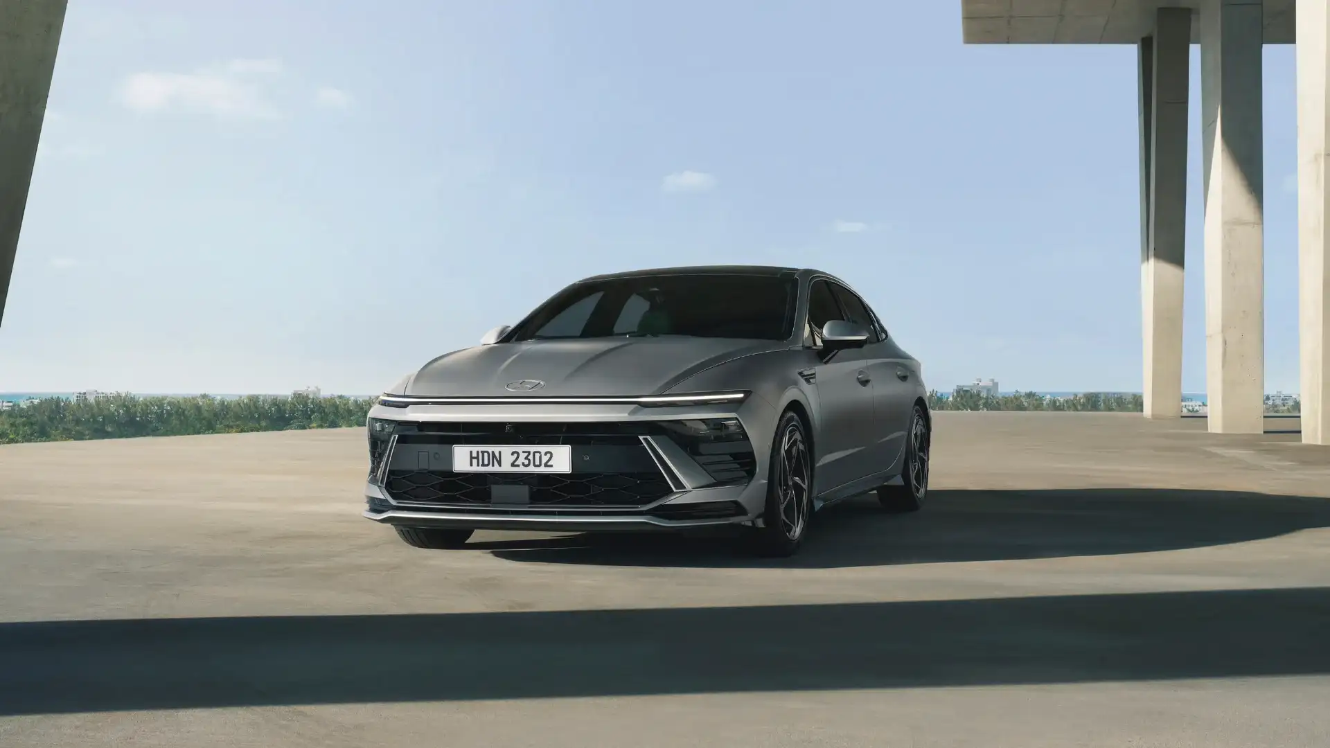 2026 Hyundai Sonata silver sedan parked under modern concrete structure with sleek front lighting.