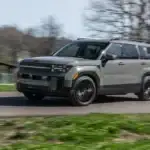 2026 Hyundai Santa Fe gray SUV driving on a curved rural road with black wheels and roof rails.