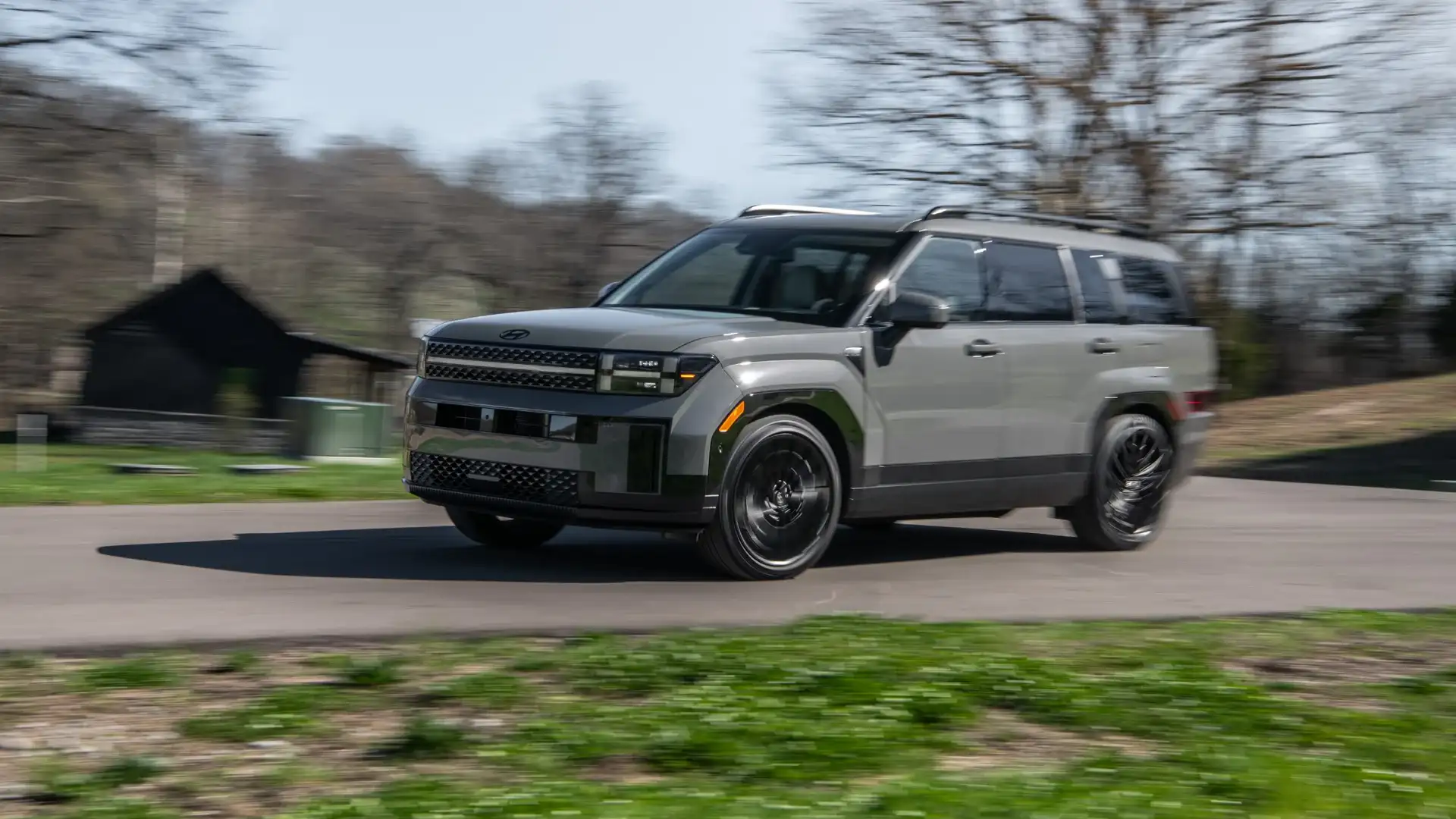 2026 Hyundai Santa Fe gray SUV driving on a curved rural road with black wheels and roof rails.