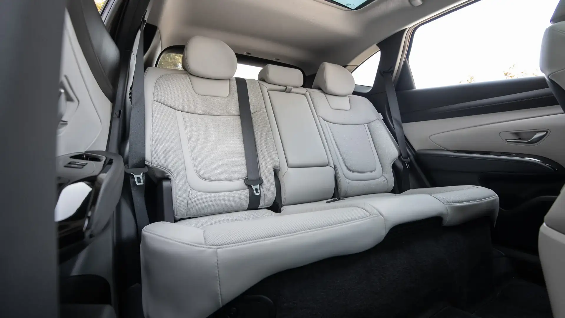 2026 Hyundai Tucson Hybrid rear cabin with light upholstery, seatbelts, and panoramic roof.