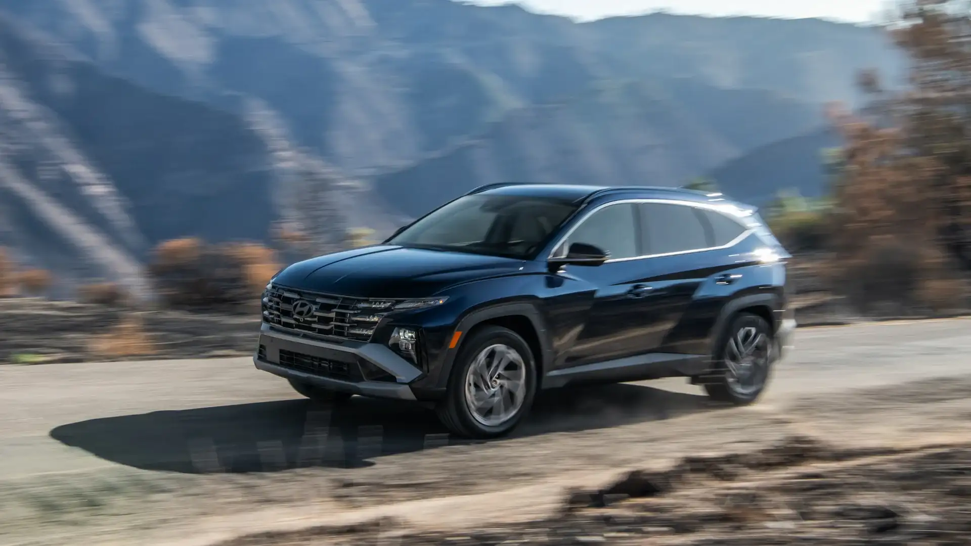 2026 Hyundai Tucson Hybrid black SUV driving through mountain road with motion blur background.
