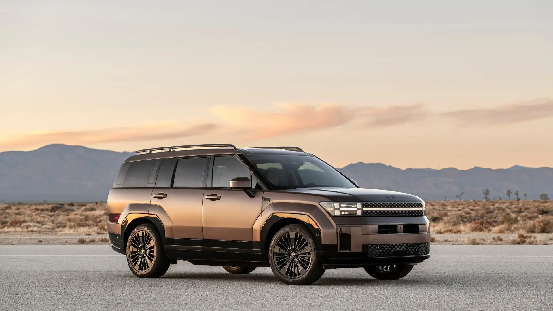 2026 Hyundai Santa Fe Hybrid bronze SUV parked on desert road at sunset with mountain backdrop.
