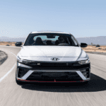 2026 Hyundai Elantra N white sport sedan driving on racetrack with front view and red trim.
