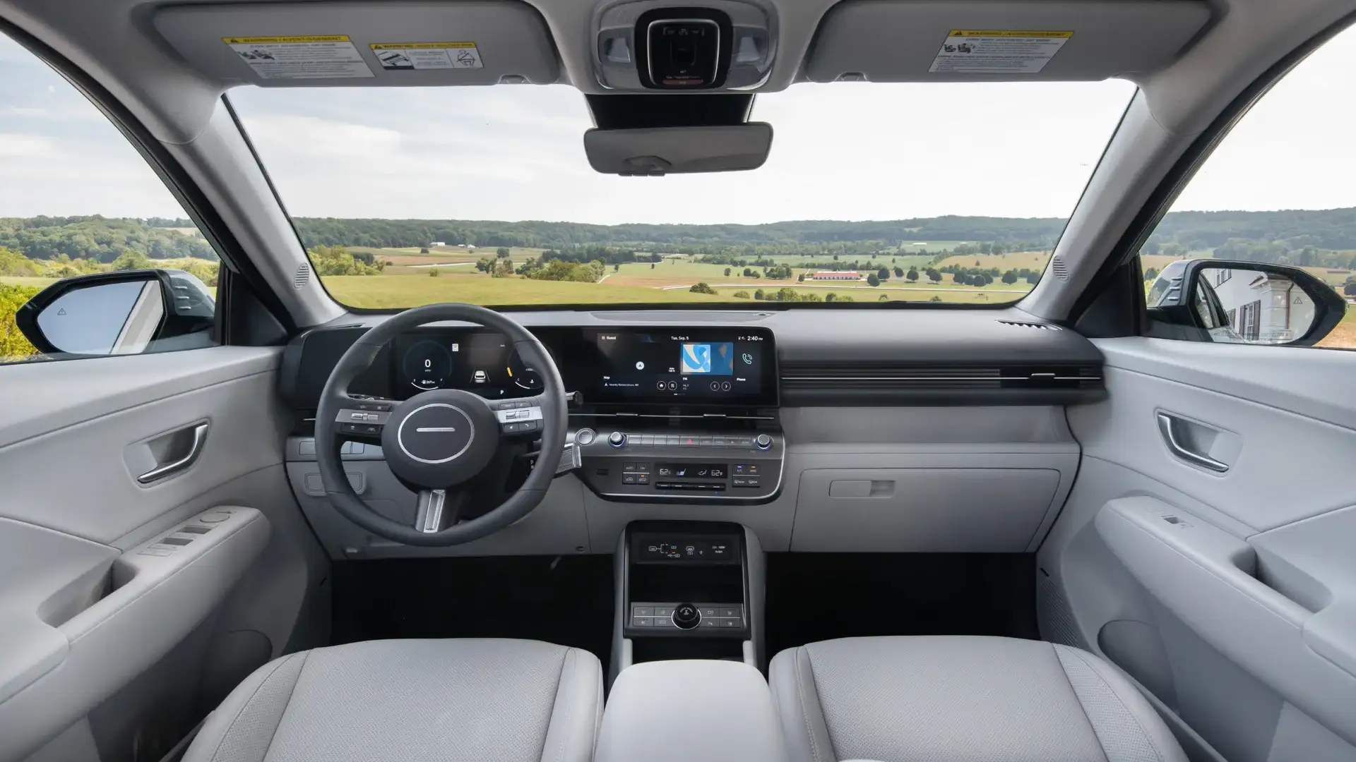 2026 Hyundai Kona light gray interior with digital display, steering wheel, and open countryside view.