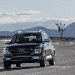 2026 Hyundai Venue black compact SUV driving on open road with mountain landscape in background.