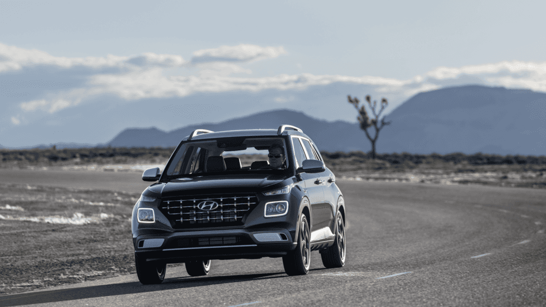 2026 Hyundai Venue black compact SUV driving on open road with mountain landscape in background.