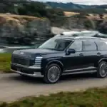 2027 Hyundai Palisade black SUV driving along coastal road with ocean cliffs and mountain backdrop.