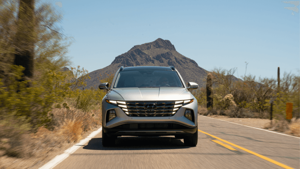 Front view of the 2025 Hyundai Tucson Hybrid driving on a desert road with mountain backdrop.