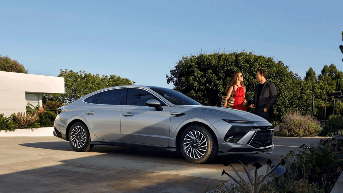 2025 Hyundai Sonata in silver parked in a modern driveway with couple standing nearby.