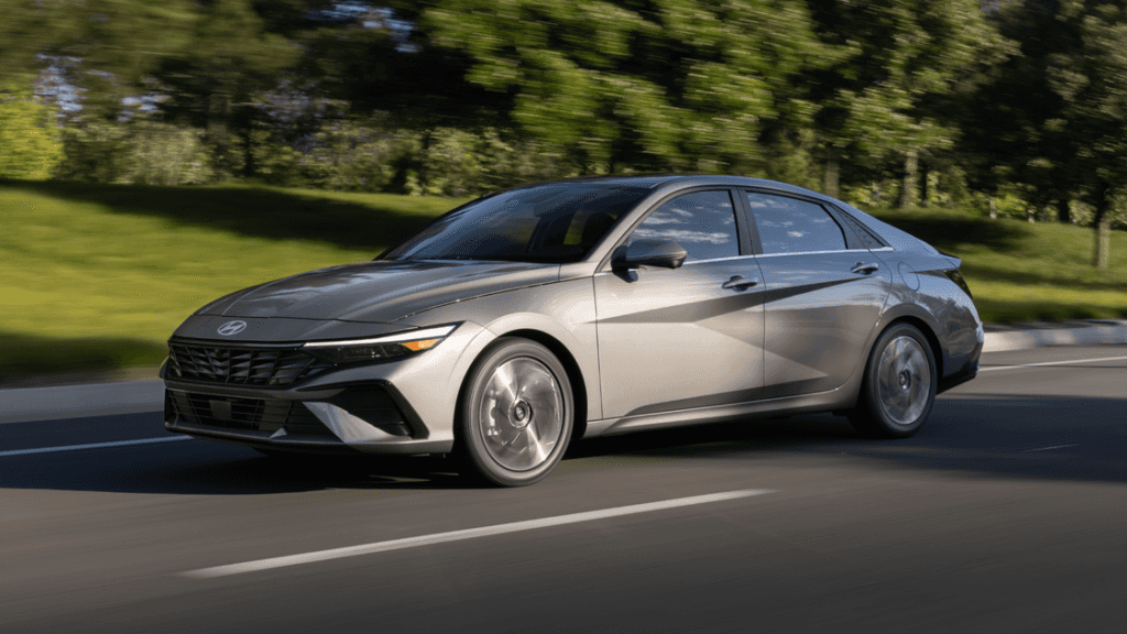 2025 Hyundai Elantra sedan in silver driving on a tree-lined road in daylight.