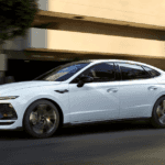 2025 Hyundai Sonata in white driving through city street with modern blacked-out roof.