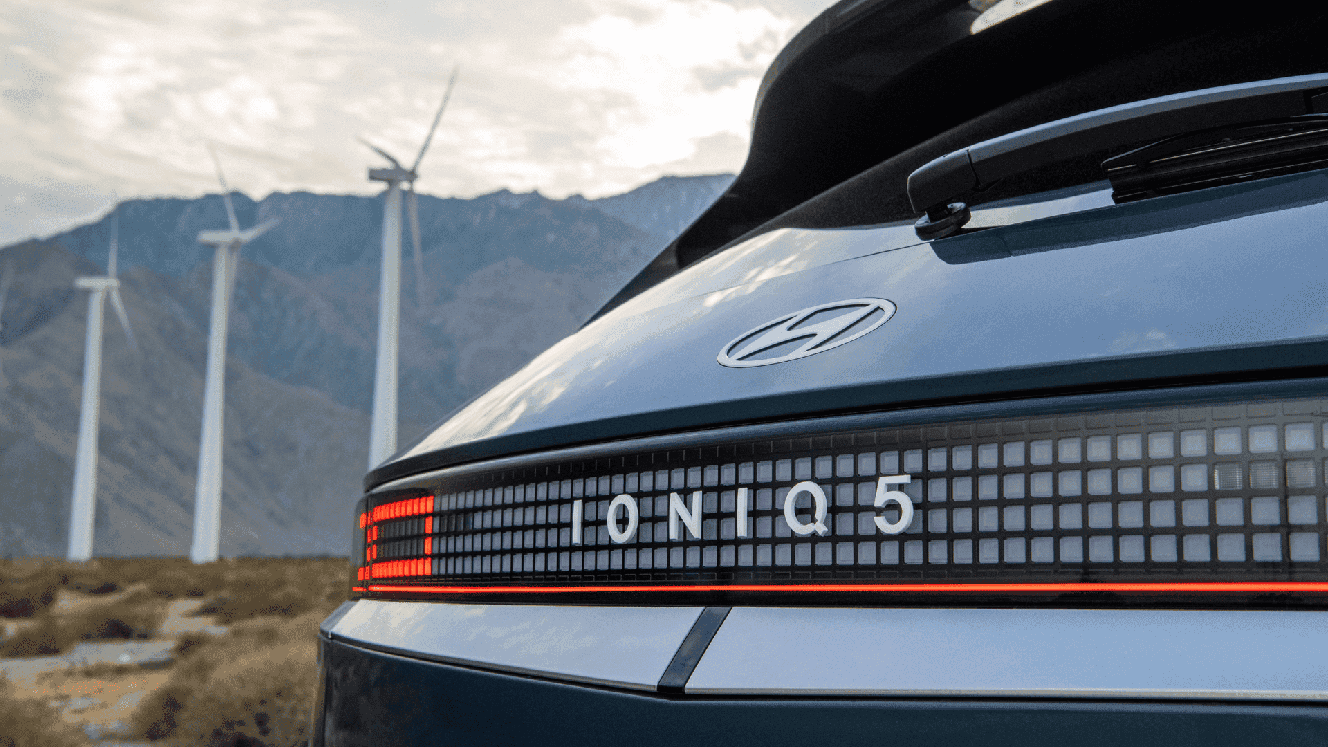 Close-up of 2025 Hyundai IONIQ 5 pixel-style rear lightbar and emblem with wind turbines in background.