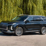 2025 Hyundai Palisade in black driving on a sunny road with lush green trees in the background