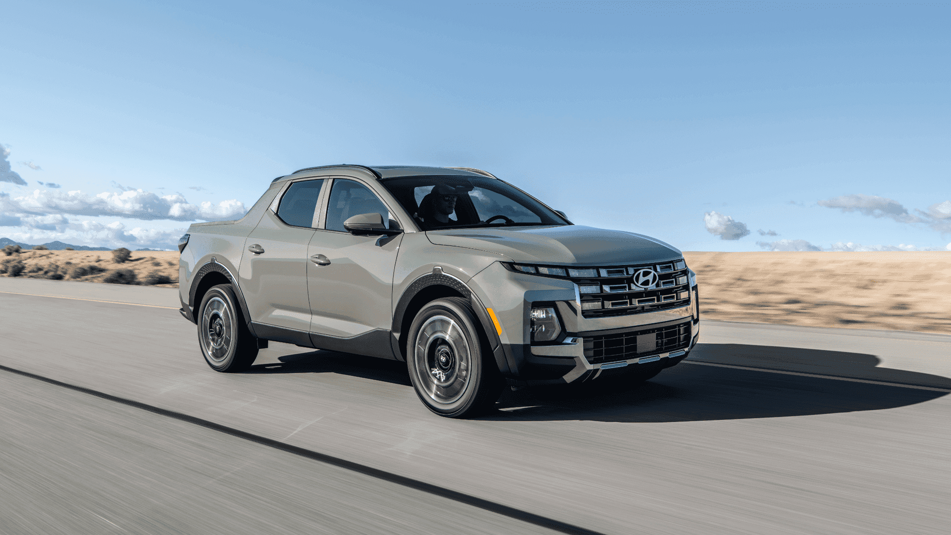 2025 Hyundai Santa Cruz compact pickup in light gray driving on open road with desert background