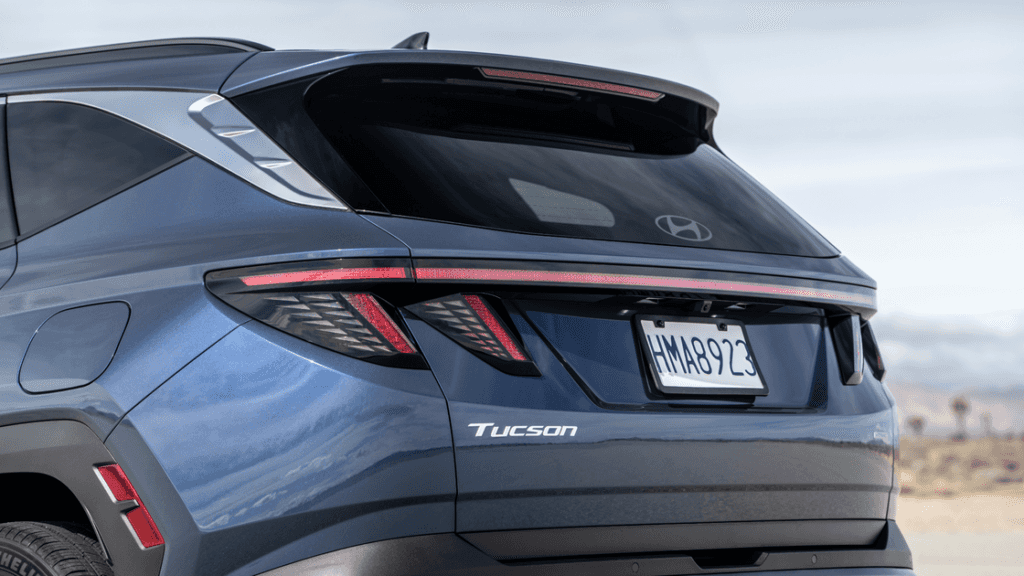 Rear view of 2025 Hyundai Tucson in blue showing LED taillights, Tucson badge, and roof spoiler.