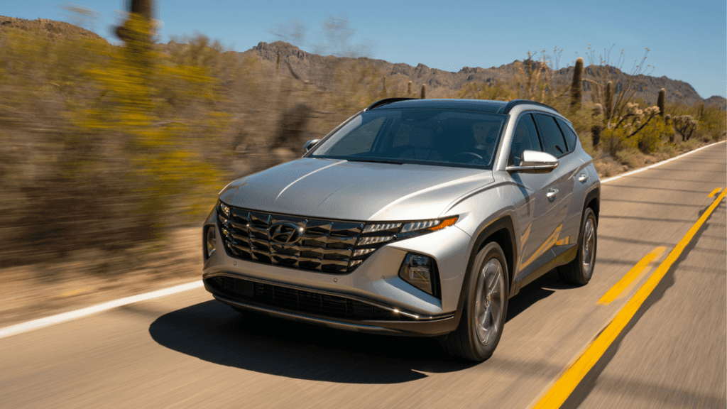 Front view of 2025 Hyundai Tucson Hybrid driving on highway with LED headlights illuminated.