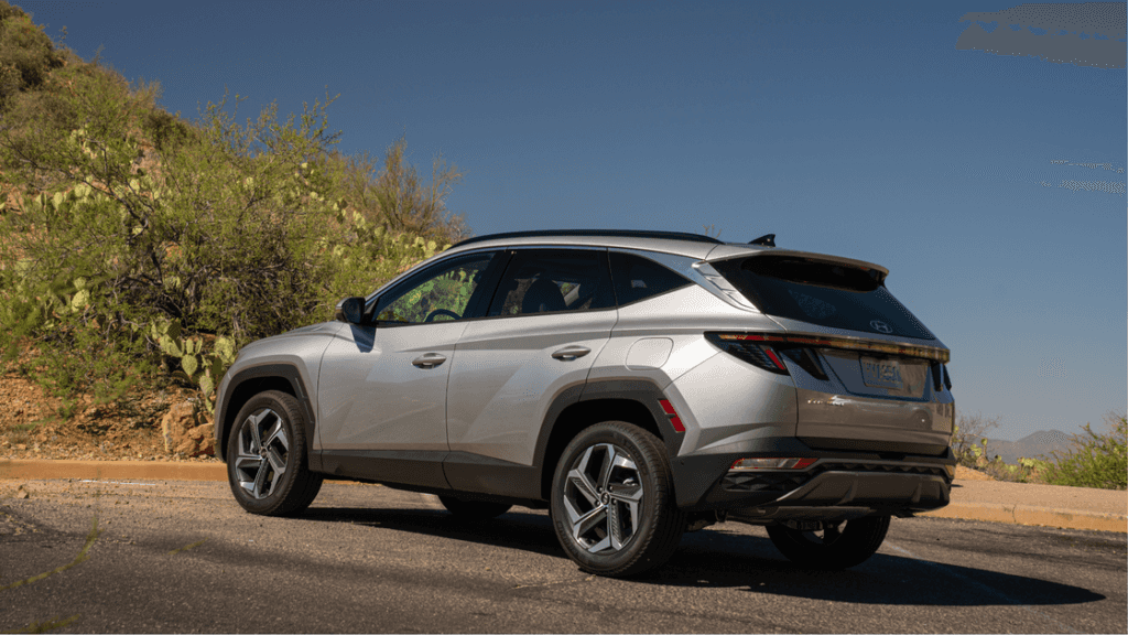 Rear angle of silver 2025 Hyundai Tucson Hybrid parked near desert terrain.