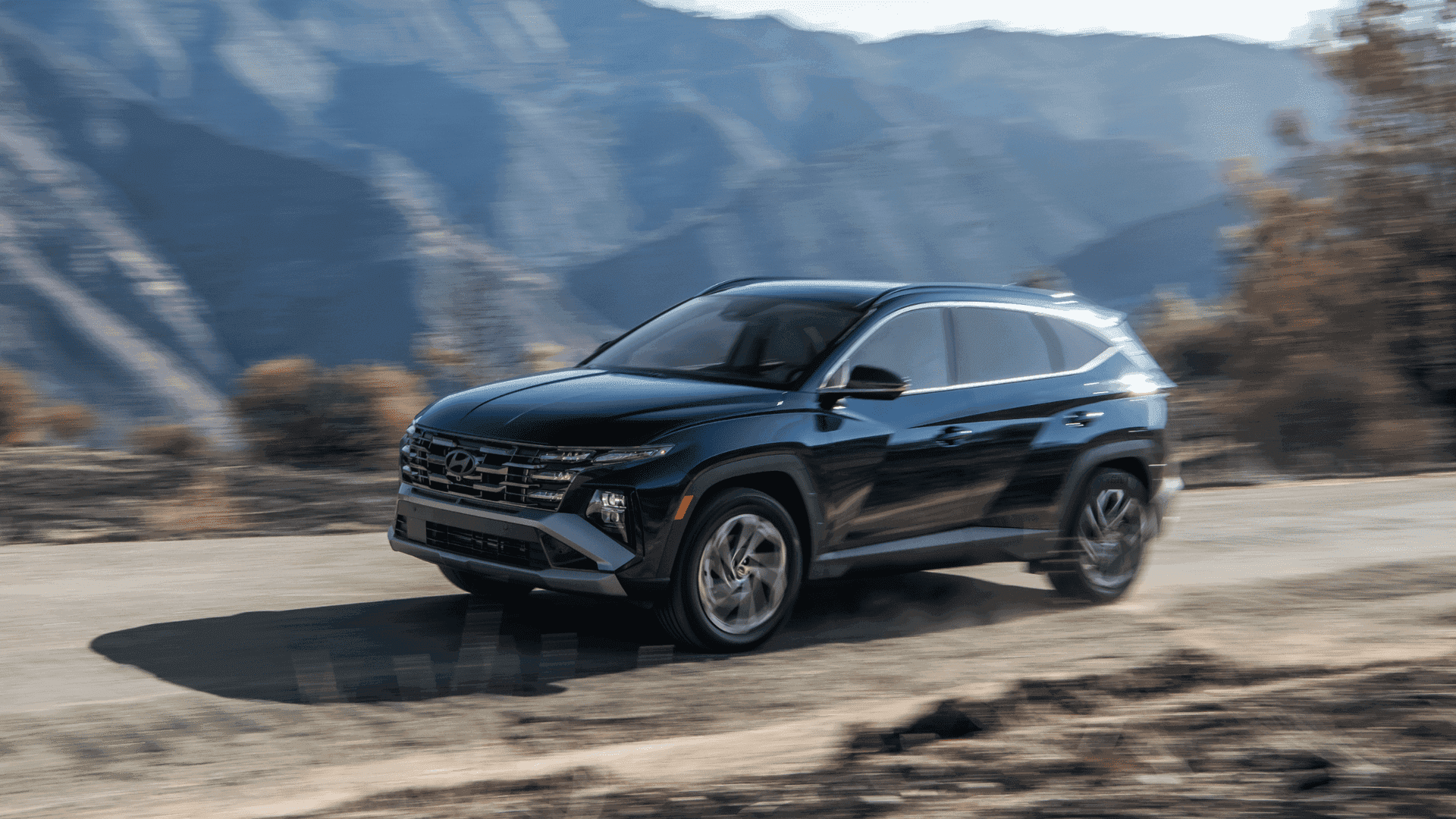 2025 Hyundai Tucson Hybrid driving fast on mountain road, showcasing bold front grille and LED lights
