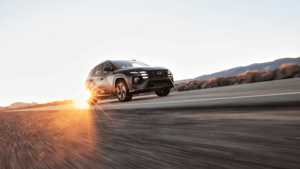 2025 Hyundai Tucson SUV driving at sunset on a desert highway with lens flare effect.