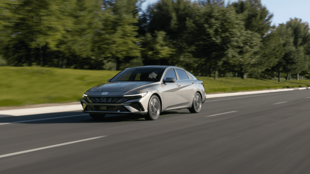 2025 Hyundai Elantra compact sedan in silver driving on suburban road with modern front-end styling.