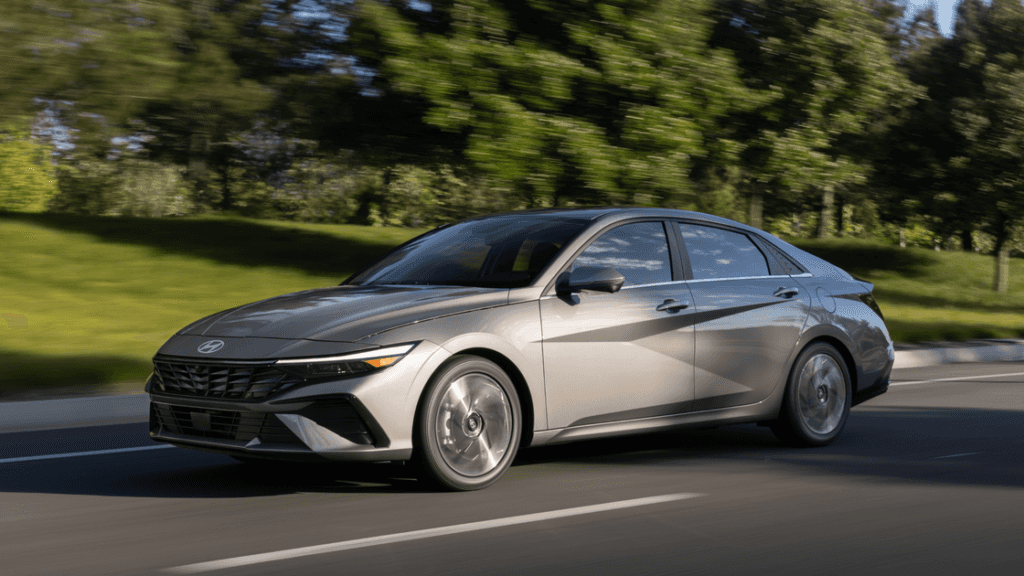 Side profile of the 2025 Hyundai Elantra in motion on a suburban road, emphasizing its sleek exterior design.