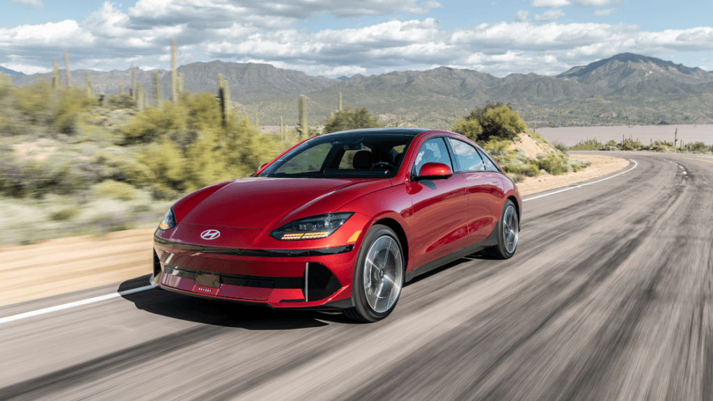 2025 Hyundai IONIQ 6 in red driving along a desert highway with mountains in the background.