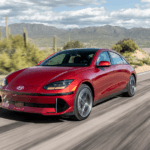 2025 Hyundai IONIQ 6 in red driving along a desert highway with mountains in the background.