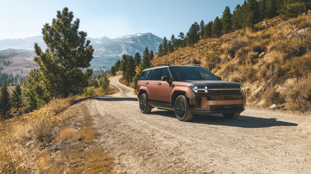 2025 Hyundai Santa Fe Hybrid in matte bronze driving on a rugged mountain road with scenic views.