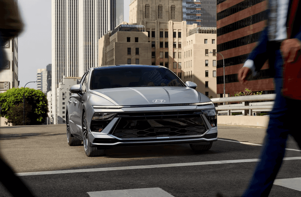 Front exterior shot of the 2025 Hyundai Sonata in silver at a city crosswalk with pedestrians nearby.