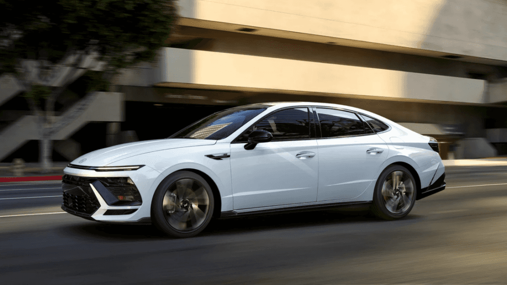 Side profile of a white 2025 Hyundai Sonata driving through city streets with modern aerodynamic styling.