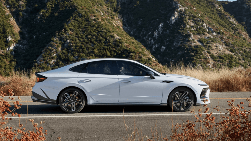 Side view of 2025 Hyundai Sonata in white parked on scenic mountain road with sleek fastback design.