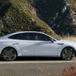 Side view of 2025 Hyundai Sonata in white parked on scenic mountain road with sleek fastback design.