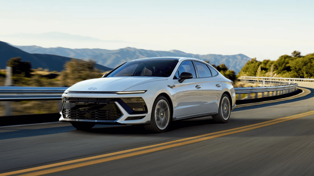White 2025 Hyundai Sonata driving on a winding road, highlighting its aggressive front-end design.