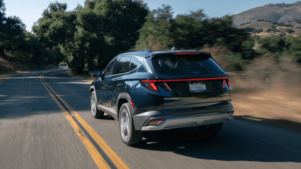 Rear view of the 2025 Hyundai Tucson Hybrid driving through a wooded road with LED taillights illuminated.