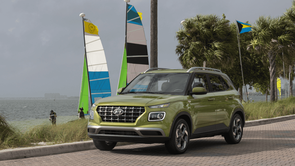 2025 Hyundai Venue in green parked near the beach with sailboats and palm trees in the background.