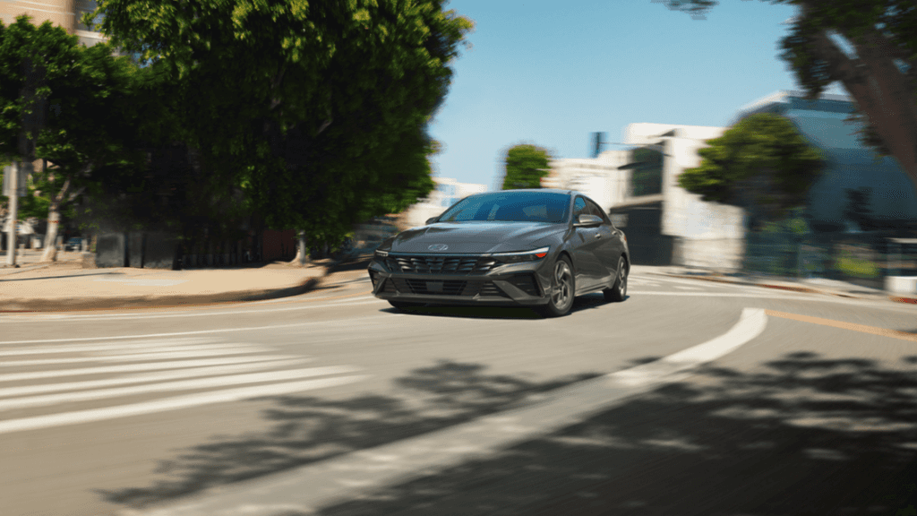 Front view of the 2025 Hyundai Elantra Hybrid in motion around a curved urban road.