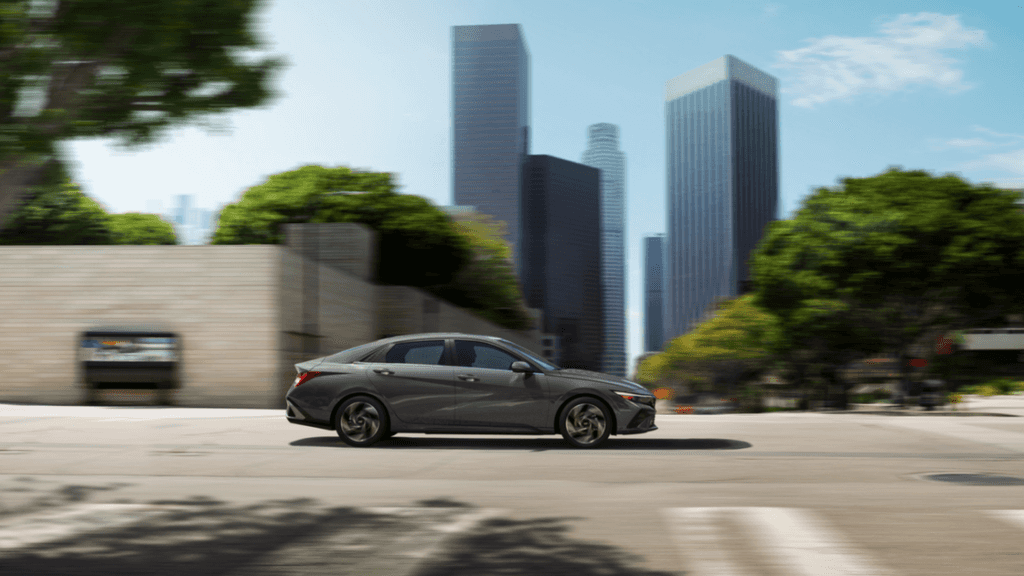Side profile of the 2025 Hyundai Elantra Hybrid driving through a modern cityscape.