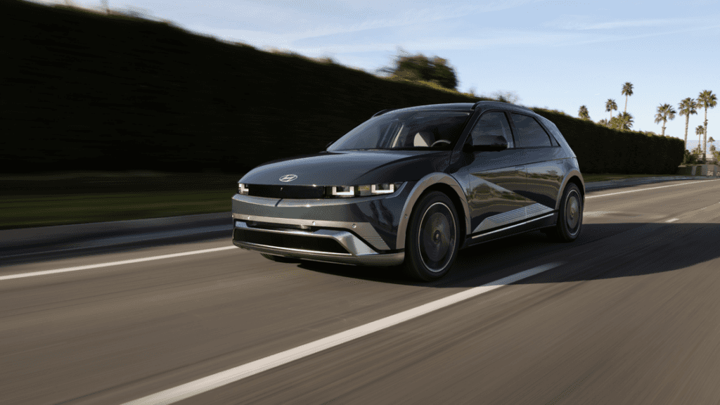 Front-angle view of a dark green 2025 Hyundai IONIQ 5 N driving on a palm-lined road in daylight.