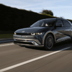Front-angle view of a dark green 2025 Hyundai IONIQ 5 N driving on a palm-lined road in daylight.