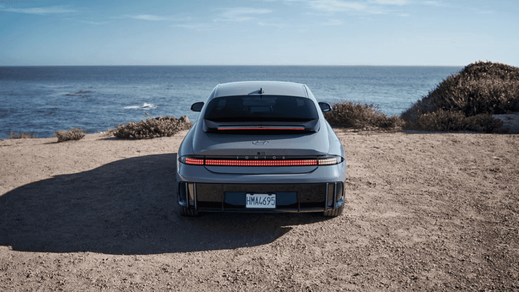 Rear view of 2025 Hyundai IONIQ 6 electric sedan parked by the ocean with LED taillights lit.